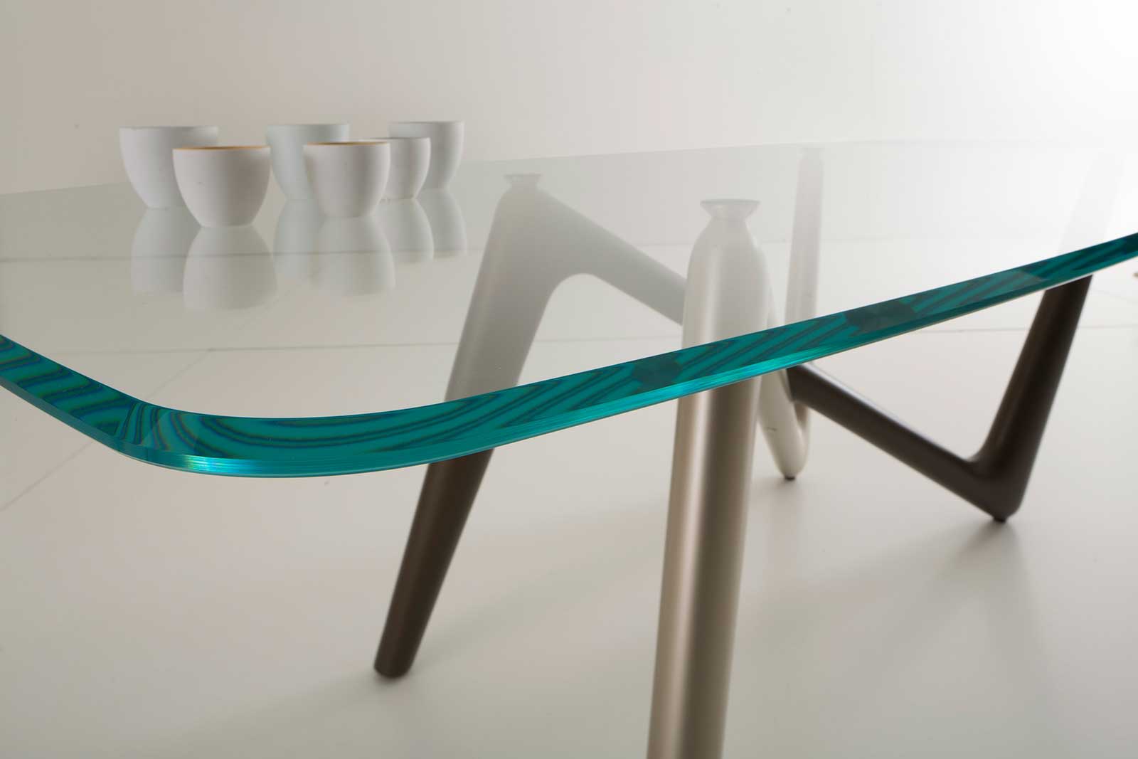 La table rectangulaire Edge a les pieds bicolore bronze et titane et le plan en verre transparent extra clair trempé de dim. cm. 110 x 220 ou 120 x 240.